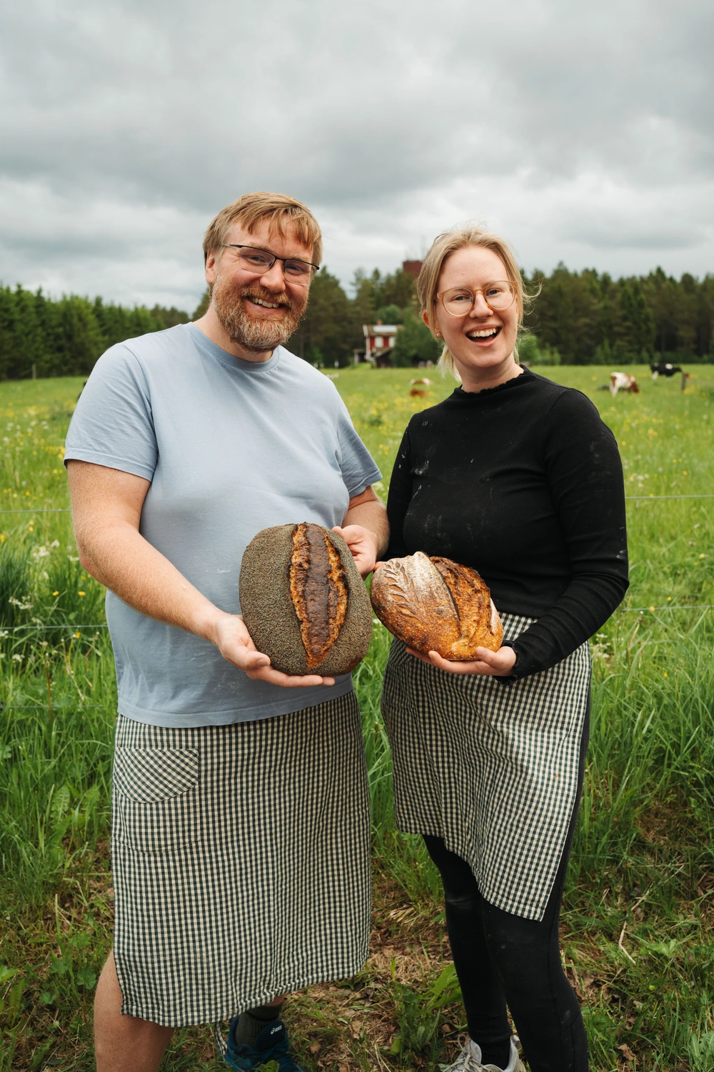 Grundarna Jesper och Maria står på en äng och håller i varsitt nybakat bröd.
